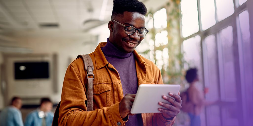 Estudante negro feliz navegando na internet em um touchpad. Monitorando despesas de viagens corporativas.