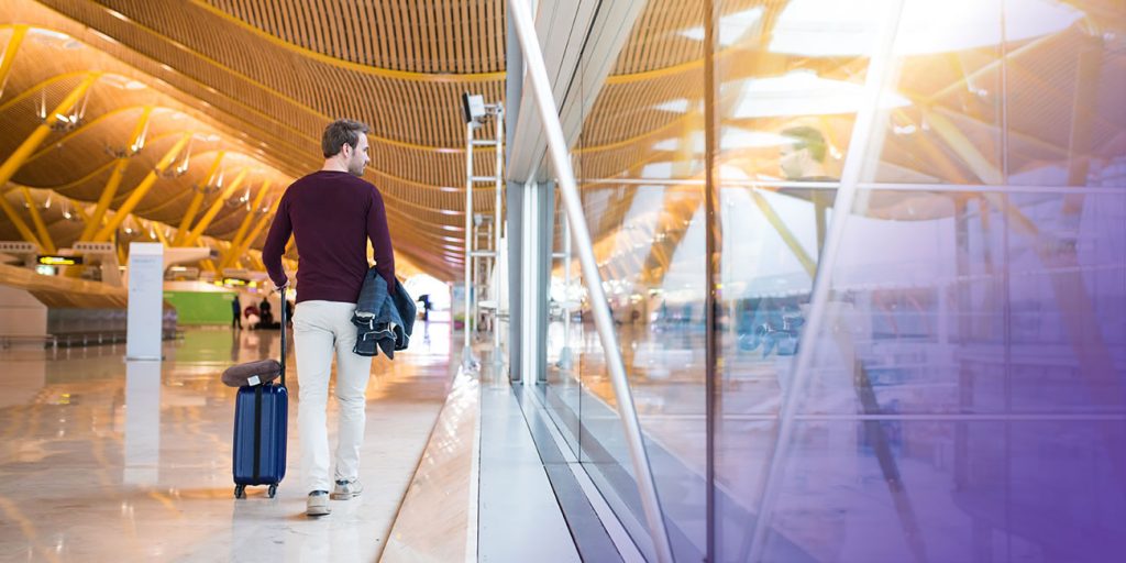Homem caminhando de costas no aeroporto. Conozca principales empresas de gestión de viajes corporativos en Colombia